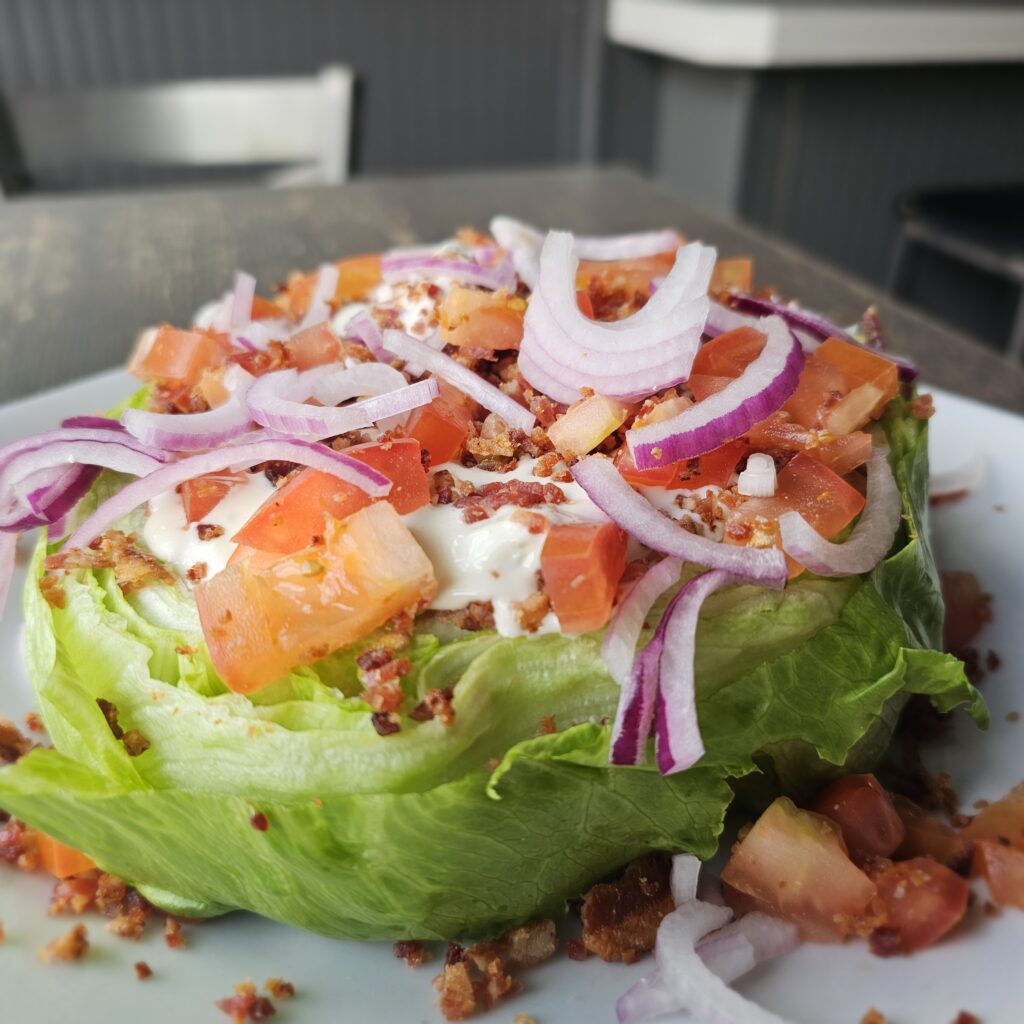 Wedge Salad: A crisp wedge of iceberg lettuce drizzled with your choice of bleu cheese or thousand Island dressing, topped with crumbled bacon, chopped red onion and tomatoes.