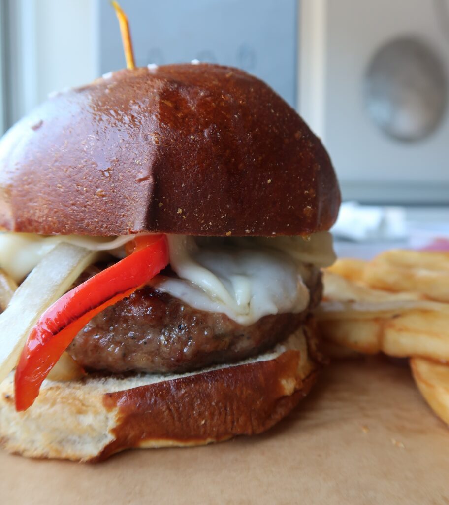 The Ballpark Burger: A savory homemade burger patty made with Sweet Italian pork Sausage & lean ground beef, grilled to perfection, with sauteed peppers & onions & sharp provolone cheese. Served on a toasted pretzel bun slathered with our homemade stone ground mustard sauce.