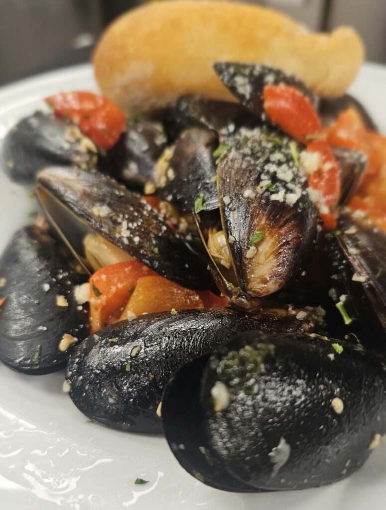 Steamed Mussels: Tender mussels steamed in garlic with red peppers & tomatoes. Served with toasted garlic bread.