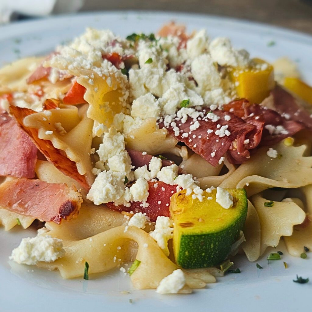 Summer Squash Sauté: Tender bowtie pasta tossed with sauteed zucchini, summer squash, Roma tomatoes, black olives, thinly sliced prosciutto with a touch of garlic and fresh basil, in a light white wine & lemon sauce sprinkled with crumbled feta cheese. 