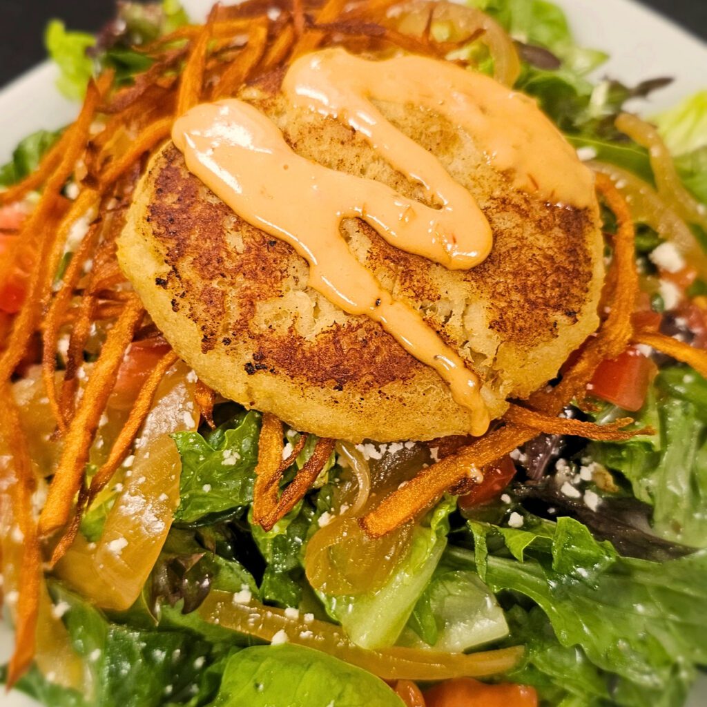 Crab Cake Salad: Mixed greens & arugula tossed in an herb-vinaigrette with avocado, marinated onions, tomato, and our signature city strings; sprinkled with queso fresco & topped with lump crab meat perfectly seared. Drizzled with thousand island dressing.