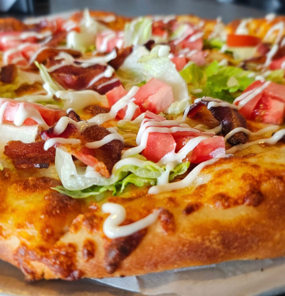 BLT Pizza: Hand stretched pizza dough, drizzled with aioli & mozzarella baked golden & bubbly, topped with a generous amount of crisp bacon, juicy tomatoes and chopped romaine lettuce. One more drizzle of creamy aioli to finish this masterpiece! Enjoy!!